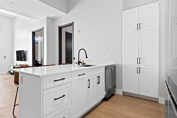 A modern kitchen with white cabinets and a wooden floor.