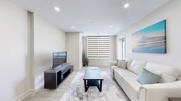A living room with a white couch, a television, and a painting on the wall.