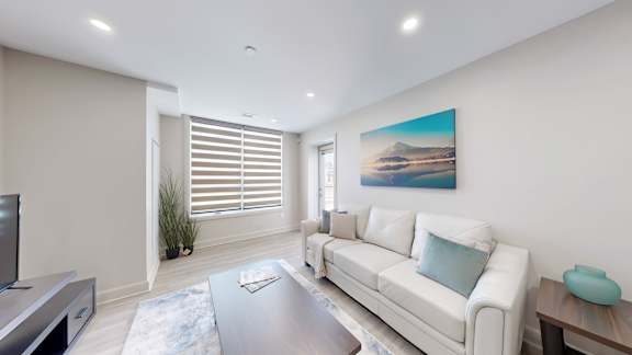 A modern living room with a white couch and a painting on the wall.