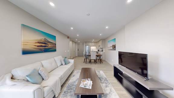 A modern living room with a white sofa and a painting of a beach scene on the wall.