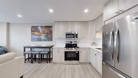 A modern kitchen with a stainless steel refrigerator and a painting of a landscape on the wall.