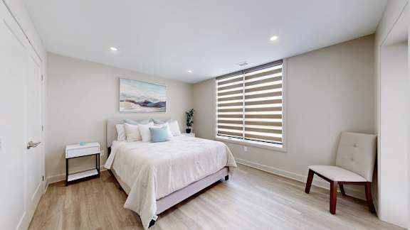 A bedroom with a large bed, a chair, and a painting on the wall.