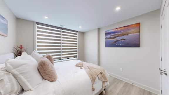 A bedroom with a bed, pillows, and a painting on the wall.