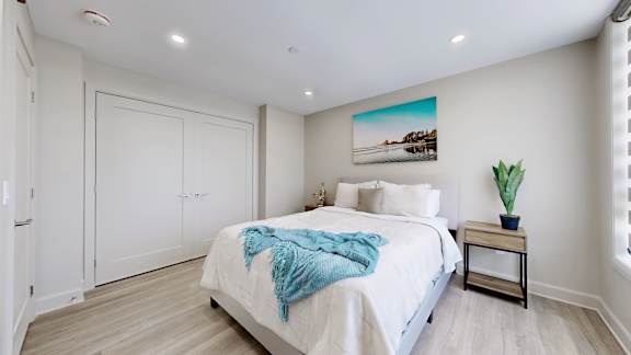 A bedroom with a bed, a plant, and a painting on the wall.