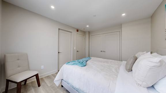 A bedroom with a bed, chair, and cabinets.