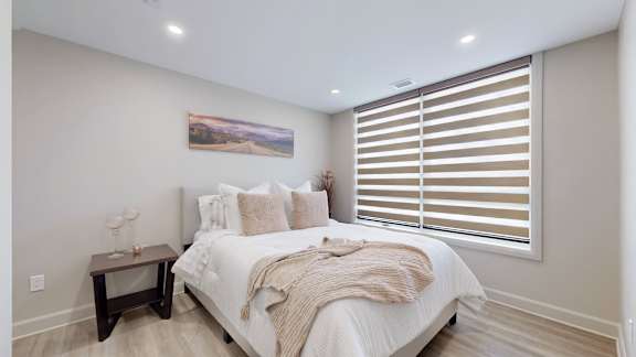 A bedroom with a large bed, a nightstand with a lamp, and a painting on the wall.