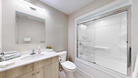 A bathroom with a toilet, sink, mirror, and a glass shower door.