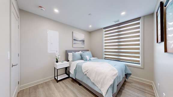 A bedroom with a bed, nightstand, and window with blinds.