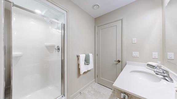 A white bathroom with a glass shower door and a white sink.