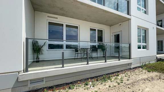 A balcony with a table and chairs is on the ground floor of a white building.