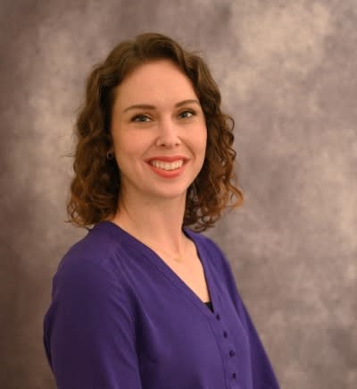 a woman in a purple shirt is smiling at the camera
