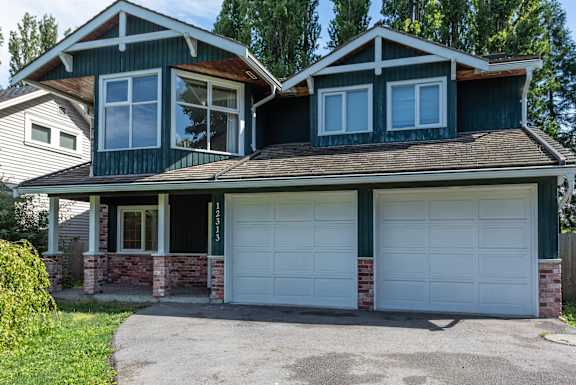 A two-story house with a green roof and white garage doors.