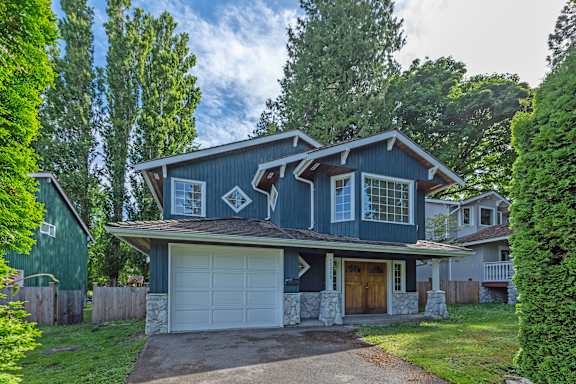 A blue house with a white garage door is surrounded by greenery.