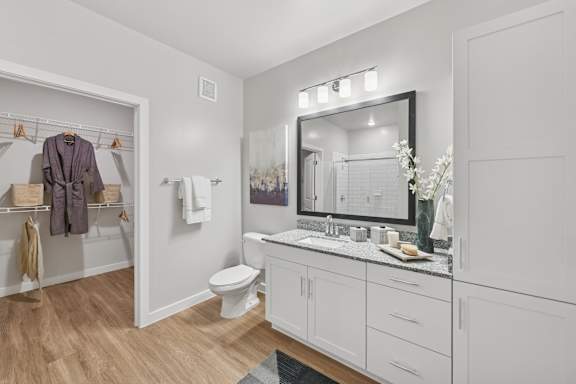 A bathroom with a toilet, sink, mirror, and wooden floors.at Allegra at Cocoa in Cocoa, FL, 32926