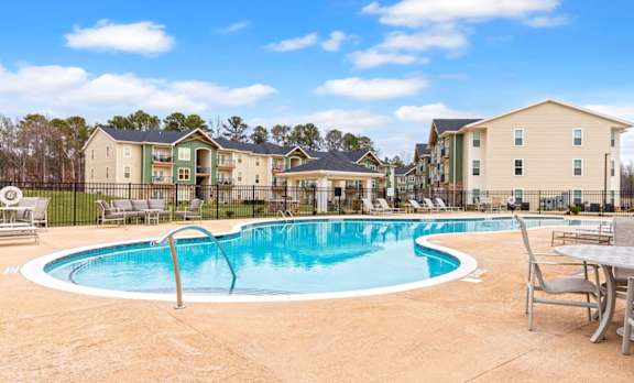 A swimming pool surrounded by chairs and tables in front of apartment buildings.