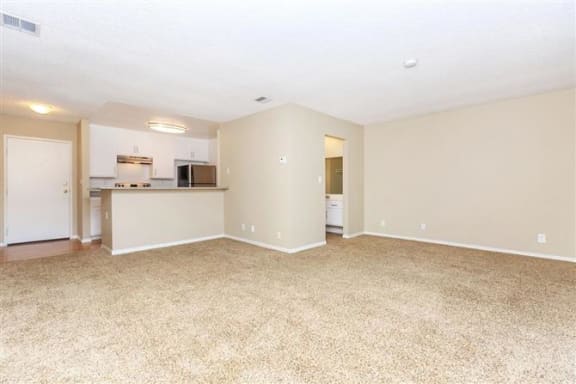 an empty living room with a kitchen in the background