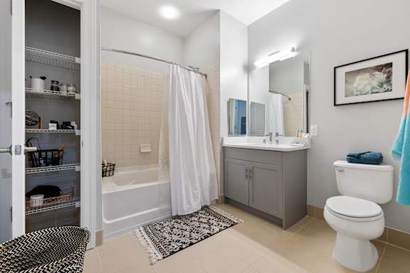 A bathroom with a white toilet, a bathtub with a white shower curtain, a sink, and a cabinet.