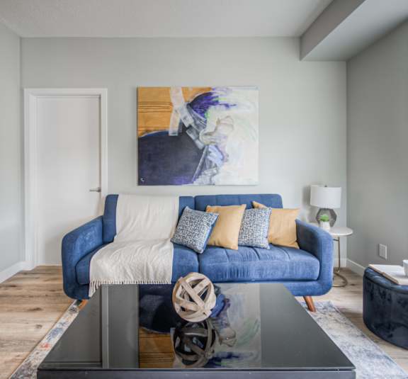 A blue couch with a white blanket and pillows sits in a room with a large painting on the wall.