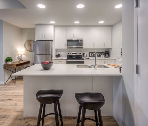 a kitchen with white cabinets and a counter with two stools