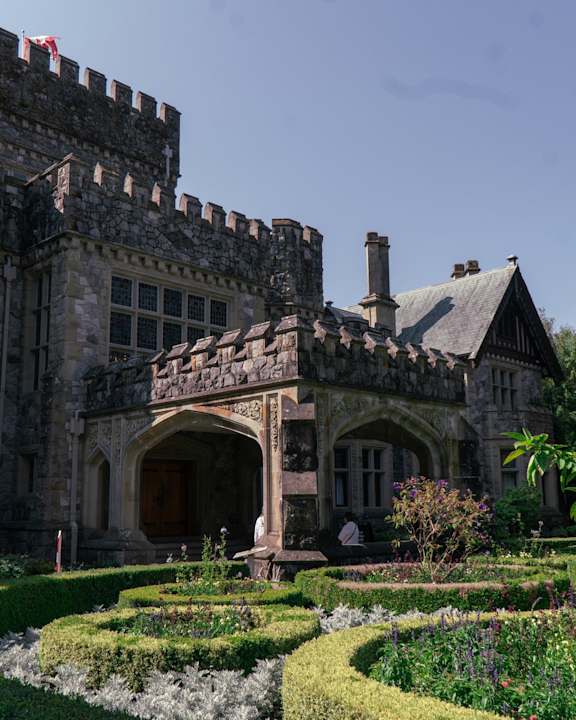 A castle-like building with a flag on top and a garden in front.