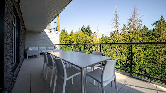 A white table and chairs are set up on a balcony with a view of trees.
