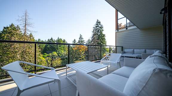 A white chair and table are on a balcony with a view of trees.