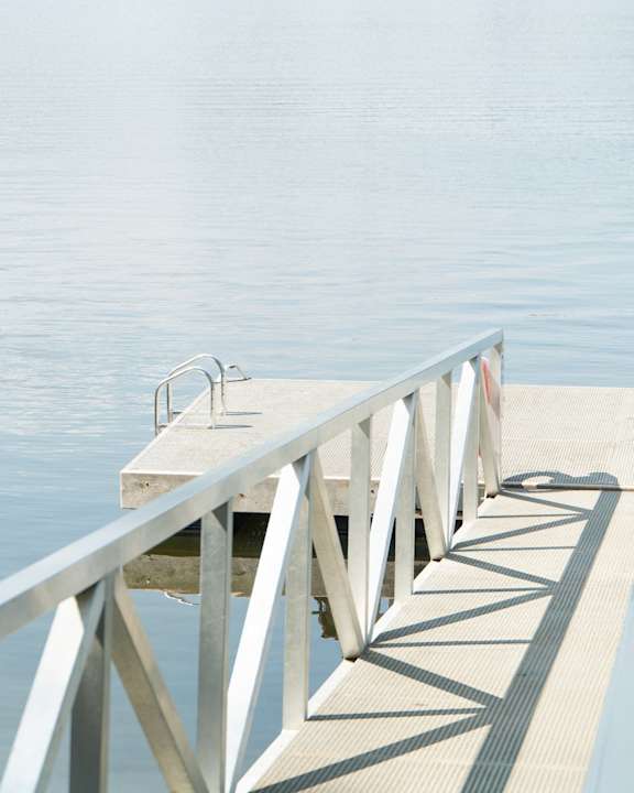 A concrete pier with metal railings extends into a calm body of water.