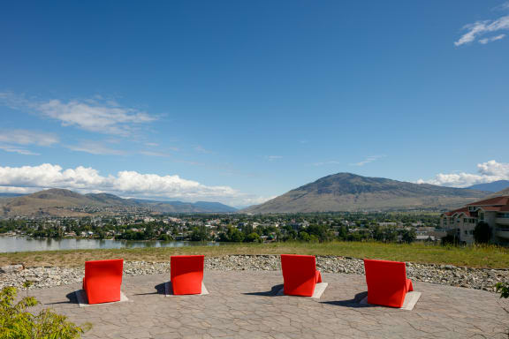 a pair of red chairs sit on a stone patio with a view of a river and mountains