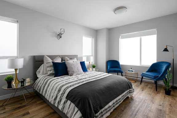 A bedroom with a bed, two chairs, and a lamp.