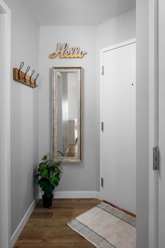 A hallway with a mirror, a plant, and a wooden floor.