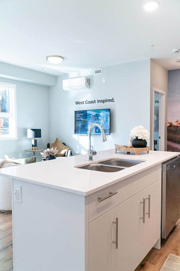 A kitchen with a white countertop and cabinets with a sign that says &quot;West Coast Inspired.&quot;.