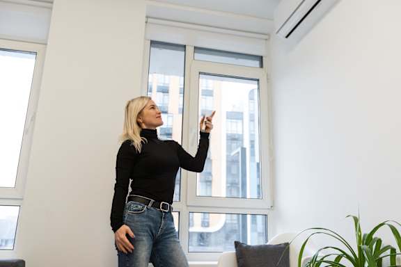 A woman in a black top and jeans is standing in a room with a large window.