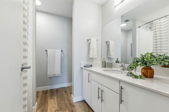 A bathroom with white cabinets and a wooden floor.