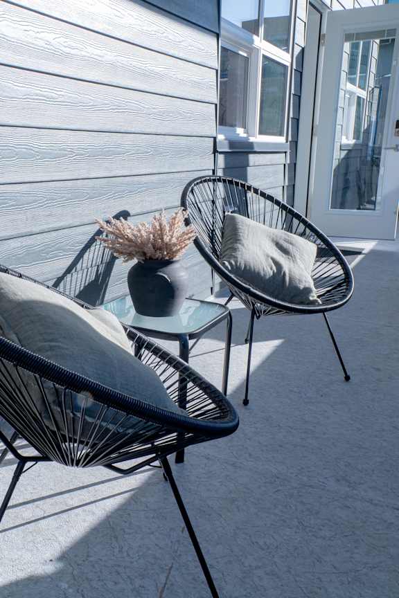 Two black wicker chairs with grey cushions are placed on a patio.