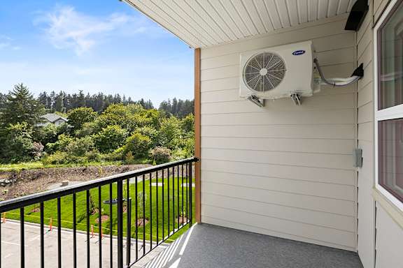 A balcony with a black railing and a white wall with a window and an air conditioner.