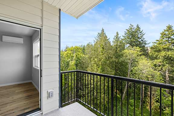 A balcony with a black railing overlooks a forest.