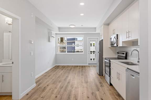 A modern kitchen with wooden floors and white cabinets.