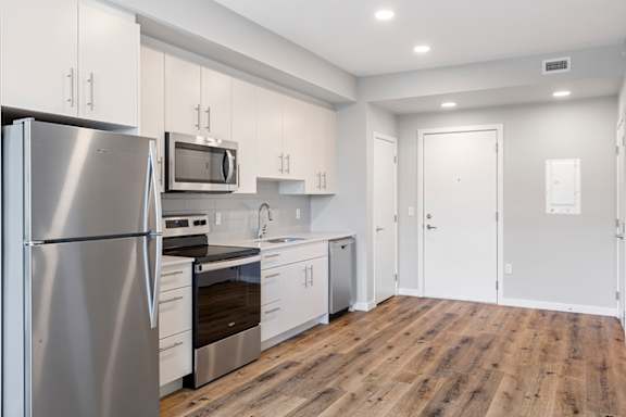 A kitchen with a stainless steel refrigerator and wooden floors.