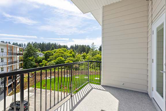A balcony with a black railing overlooks a green lawn and trees.