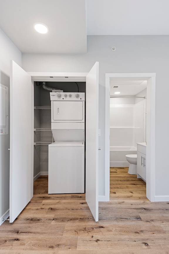 A white kitchen with a stove top oven and a toilet in the hallway.