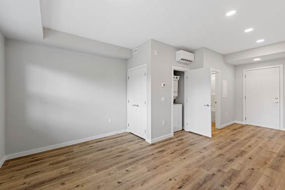 A room with wooden floors and white walls, with a door open to a hallway.