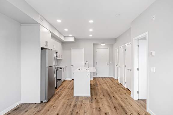 A kitchen with a refrigerator, sink, and wooden floors.