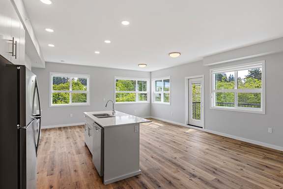 A kitchen with a refrigerator, sink, and wooden floors.
