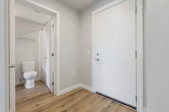 A white bathroom with wood flooring and a white toilet.