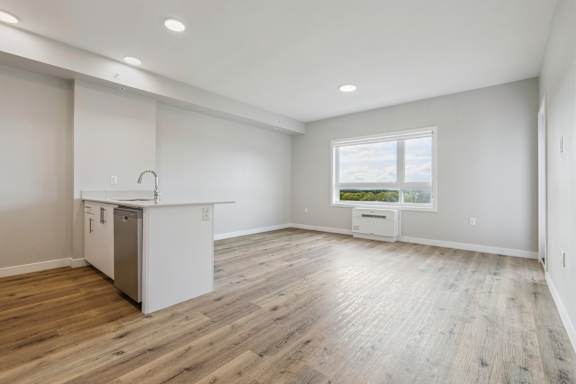 A spacious room with wooden flooring and a kitchen area with white appliances.