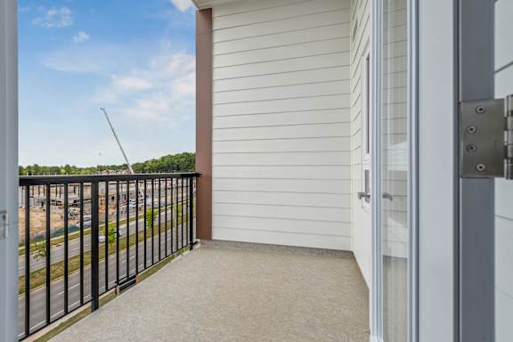 A balcony with a black railing and a view of a street and trees.
