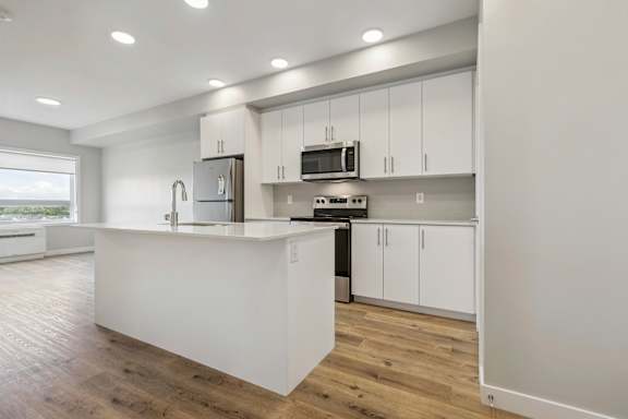 A modern kitchen with white cabinets and a wooden floor.