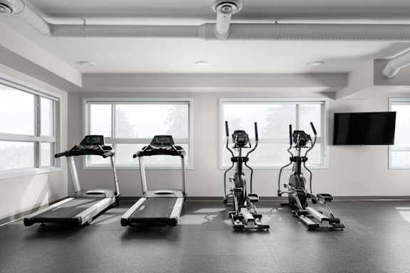 A row of treadmills and stationary bikes are lined up in a gym.