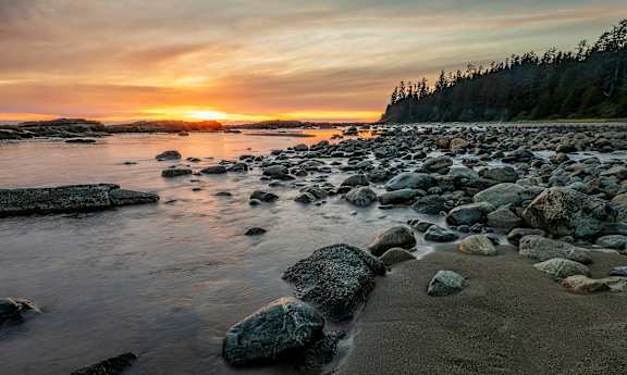 the sun sets over the rocky shore