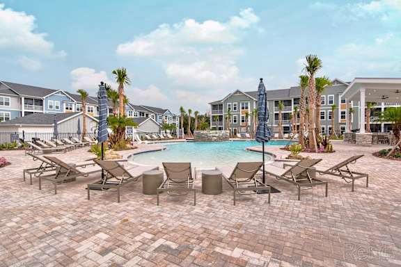 A pool surrounded by chairs and umbrellas with apartment buildings in the background at Standard441 Luxury Apartment Homes, Florida